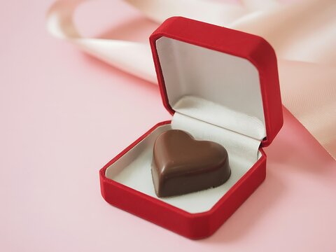 Chocolate heart shaped candy in a red gift box on pink background with ribbon