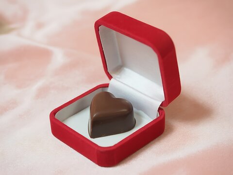 Chocolate heart shaped candy in a red gift box on pink background