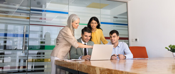 Naklejka premium Diverse businesspeople discussing project on laptop, listening to woman colleague explaining data, pointing on screen, reviewing business presentation together during corporate office briefing, banner