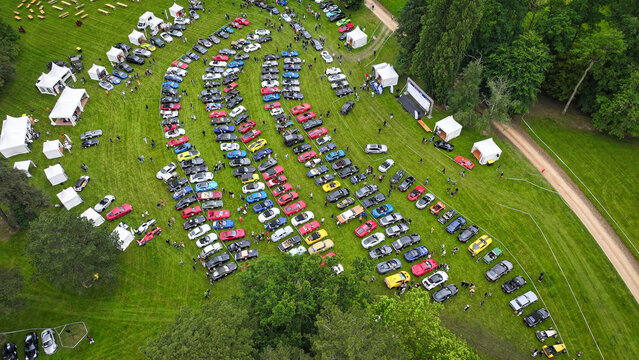 La Chapelle-de-Guinchay, France - 01 June 2024: Aerial view of rows of colorful sports cars parked on a green lawn during an outdoor automotive event with white tents.