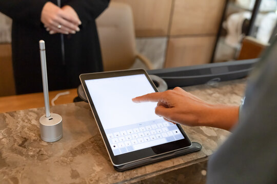 Closeup of hotel guest using tablet for digital check-in, confirming booking details, entering information, signing form digitally at reception. Customer services, check-out, travel industry concept