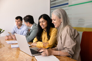 Fototapeta premium Multiethnic female colleagues working on laptop, discussing project details, reviewing data, planning strategy, team preparing business presentation, sharing ideas, collaborating in corporate office