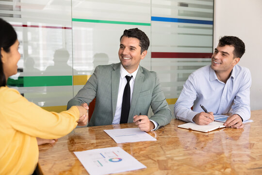 Diverse businesspeople shaking hands at conference table with financial charts, starting briefing, or finalizing negotiations, collaborative meeting in office boardroom. Teamwork, business agreement