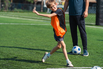 Fototapeta premium World cup concept with soccer ball or football player, young boy playing soccer on green field with coach in background