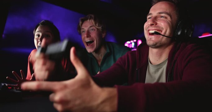 Group of young adult friends gamers celebrating victory, watching male gamer holding controller, playing video game in cybercafe, closeup. Concept of cybersport, hobby, online recreational activity