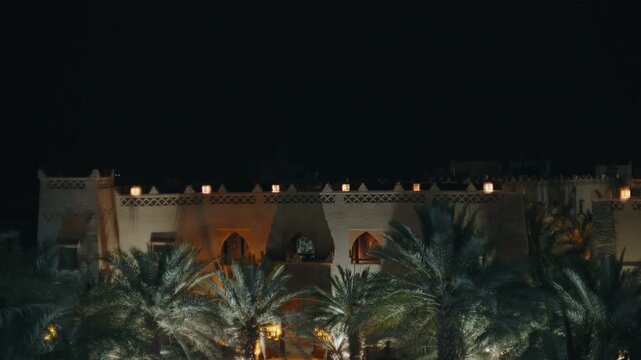 Lit kasbah walls with arched doorways and palm grove at night in Moroccan oasis town