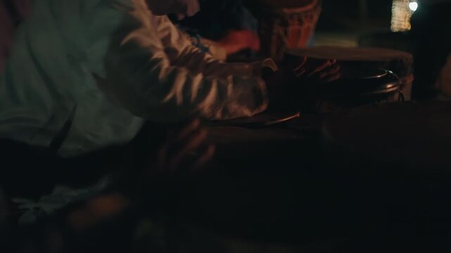 Hands drumming on traditional frame drums beside campfire at night in Moroccan desert