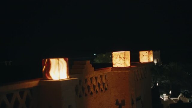 Illuminated stone lanterns lining ornate kasbah wall at night in Moroccan oasis