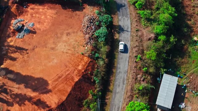 car moving along a narrow curved road with red tiled roofing houses and surrounding trees in rural area at coorg, karnataka, india. day time, trucking shot, drone shot, top down shot, 4k.