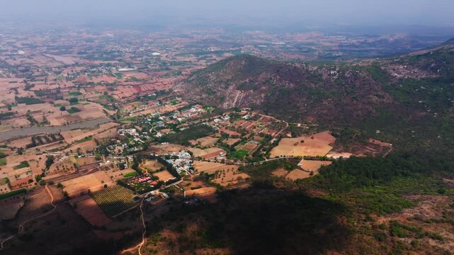 Aerial view of farming lands with small villages with haze and cloud shadows near nandi hills at Bangalore, karnataka, india. day time, semi orbit shot, drone shot, 4k.