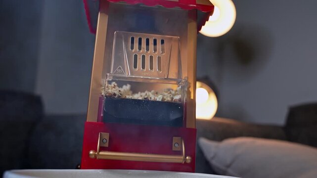 a vintage red popcorn machine actively popping fresh kernels in a cozy living room with soft bokeh lighting. Ideal for home entertainment and movie night lifestyle content.