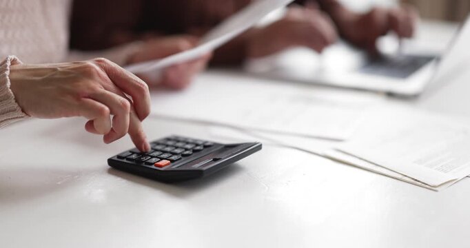 Closeup wife holding bills using calculator, sits at table with husband making payments through e-banking system on laptop. Household finances management, family budgeting financial planning concept