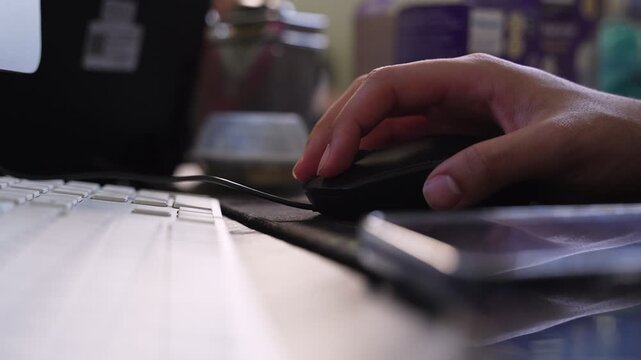shot of a person's hand using a black computer mouse on a desk with a white keyboard. The scene captures digital work, professional productivity, and office technology.
