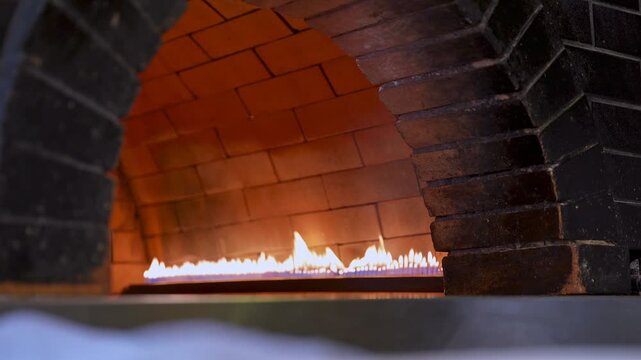 Static shot of an empty brick oven interior as orange flames burn along the back wall. Professional gas heating for bakery or pizzeria kitchen equipment.
