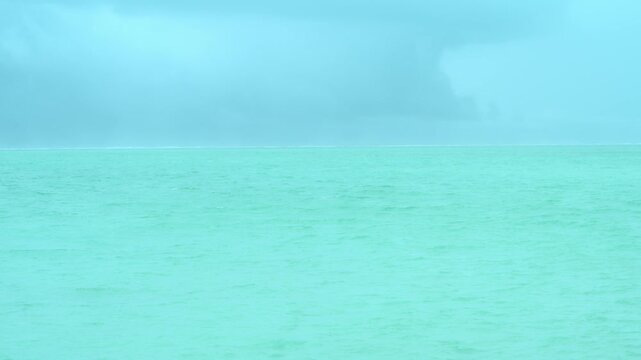 曇り空の下に広がるエメラルドグリーンの海と水平線のミニマルな風景