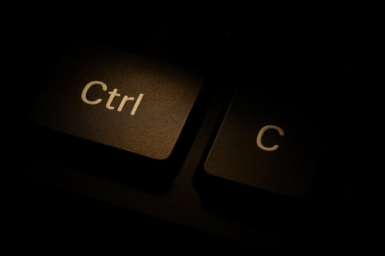 Close up of illuminated keyboard key with dramatic lighting on dark background, control key and C letter highlighted with warm glow, shallow depth of field