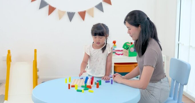Asian single mother guiding preschool daughter arranging colorful counting rods on board at table, hands-on home learning game strengthening logic, coordination, patience, child development support