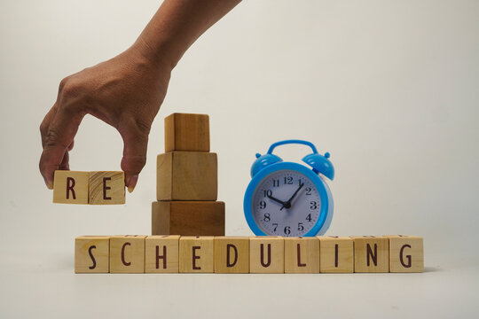 Hand Placing RE Wooden Blocks for Rescheduling Concept with Alarm Clock for Time Management and Business Planning