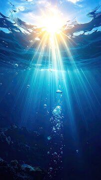 Brilliant sunrays pierce through the clear blue ocean, illuminating rising bubbles and the mysterious seabed below.