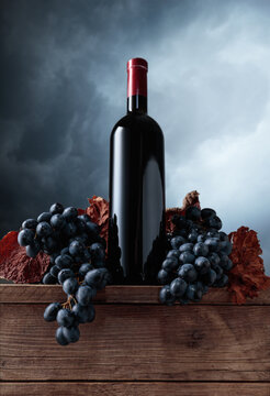 Red wine bottle with blue grapes on an old wooden table.