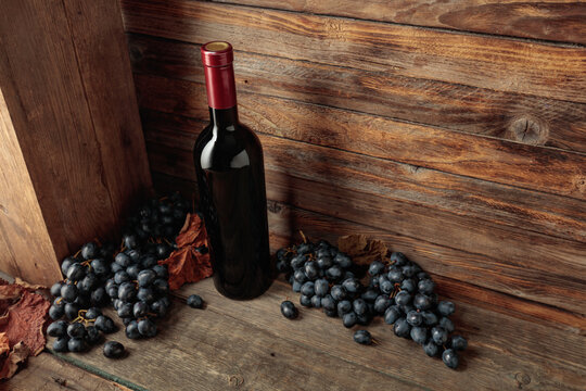 Red wine bottle with blue grapes on an old wooden table.