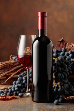 Bottle of red wine with blue grapes on a brown background.