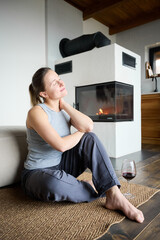 Naklejka premium Woman unwinding near fireplace with wine in hand, sitting on floor and enjoying peaceful, warm and inviting interior setting