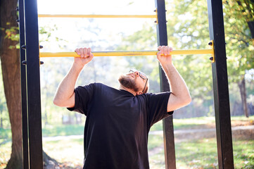 Obraz premium Man performs pull up on horizontal bar at outdoor gym in park. Active fitness scene for strength training, calisthenics, healthy lifestyle, sports motivation, or workout promotion