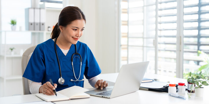Doctor looking at laptop screen writing in notebook for research planning or medical tech innovation in hospital office. Healthcare medic worker, research.