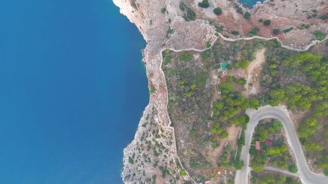 Alanya, Turkey. Medieval Seljuk fortress wall crowning a rocky Mediterranean peninsula, top-down aerial drone view with winding modern asphalt road below under summer sun. Aerial View, HEAD OVER SHOT