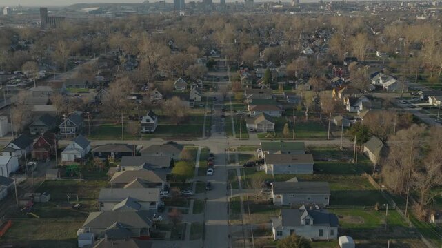 Aerial forward flight with tilt up reveal over North Omaha Nebraska neighborhood transitions from close rooftop view to wide panorama of downtown Omaha skyline at golden hour