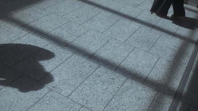 Passengers walking with rolling luggage inside Montparnasse station in Paris, filmed from overhead perspective with visible shadows on the floor