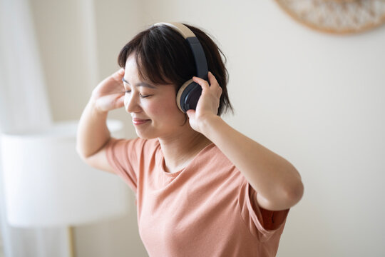 部屋でヘッドフォンをして音楽を聴いている女性