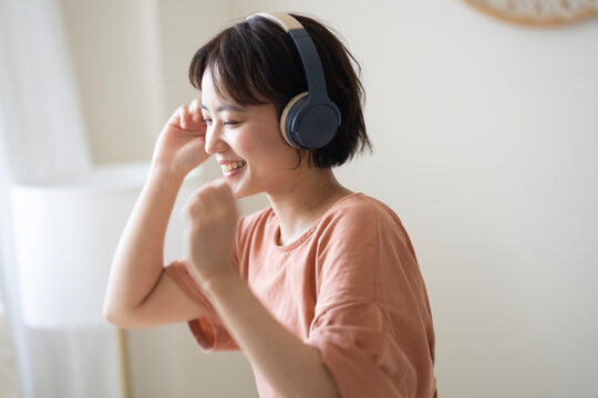 部屋でヘッドフォンをして音楽を聴いている女性