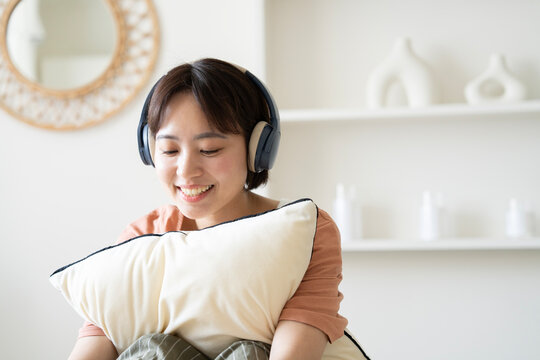 部屋でヘッドフォンをして音楽を聴いている女性