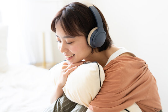 部屋でヘッドフォンをして音楽を聴いている女性
