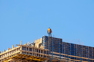 Naklejka premium Construction worker on scaffolding at high-rise building site under clear sky