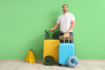 Young handsome man with suitcases, travel pillow and flippers near green wall © Pixel-Shot