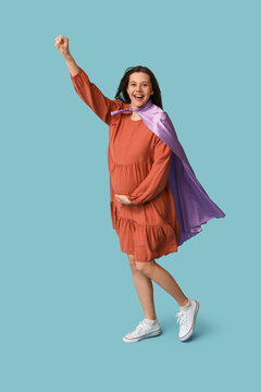 Happy young pregnant woman in superhero cape on blue background