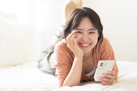 ベッドに寝そべってスマホを持っているショートカットの女性