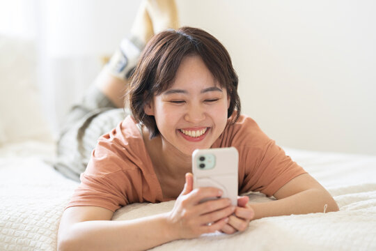 ベッドに寝そべってスマホを持っているショートカットの女性