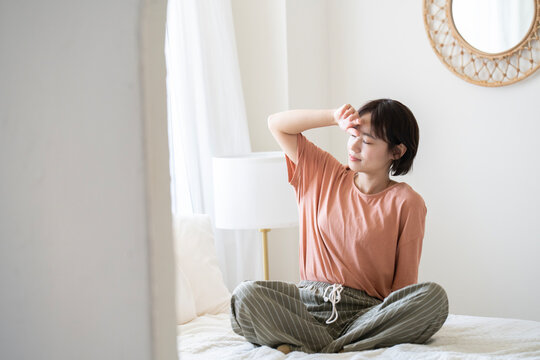 ベッドにあぐらをかいて眩しそうにしているショートカットの女性