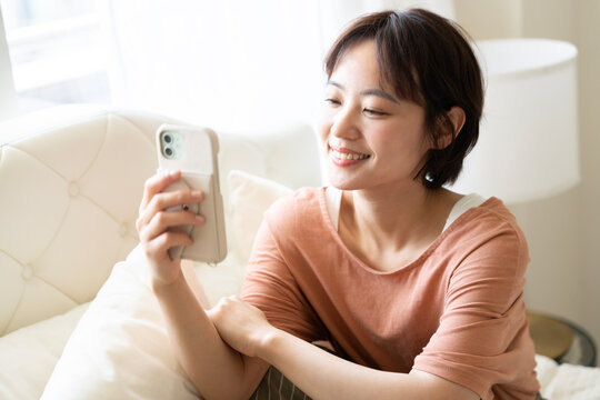 部屋でスマホを操作しているショートカットの女性