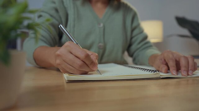Close-up image of a woman's hand holding a pen and writing on a surface, possibly a notebook or a desk.