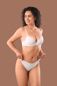 Beautiful young happy African-American woman with stretch marks on her body against beige background