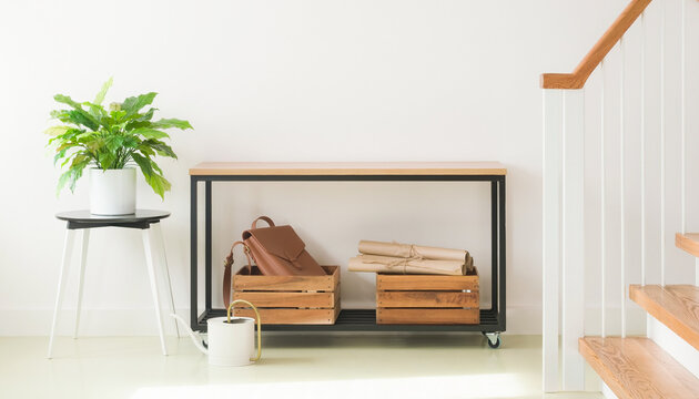 Minimalist wooden console table against white wall featuring decorative crates and green plant on side stool.