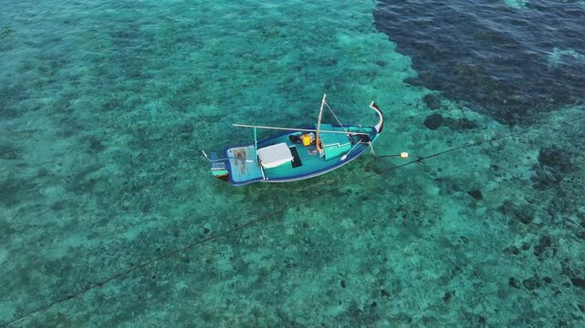Aerial view of a traditional Maldivian dhoni boat anchored in crystal clear turquoise water over a coral reef Vashafaru, Haa Alif, Maldives.