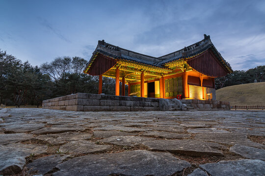 Traditional Korean pavilion illuminated at twilight with stone pavement and blue hour sky