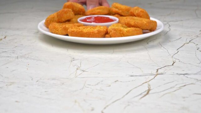 A hand serving a white plate of chicken nuggets with ketchup