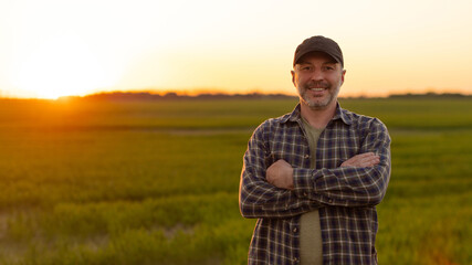 Smiling farmer with crossed arms standing in green farmland at sunset © Home-stock